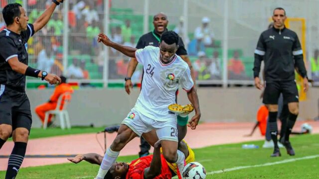 Ben Stanley Omondi challenges a Guinea player as Benni McCarthy watches